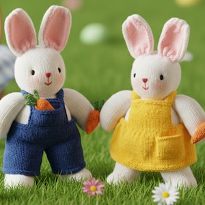May include: Two knitted white bunny dolls with pink-lined ears, holding carrots. One wears blue overalls, the other a yellow apron. They stand on green grass with Easter eggs and flowers, suggesting a spring theme.