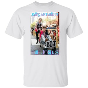 May include: White t-shirt featuring a graphic of two people, one pushing the other in a small cart. The graphic includes the text "Department of Jocks" in a colorful font. The image is set against a street scene.