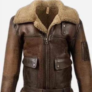 Könnte beinhalten: Braune Lederjacke mit Lammfellkragen und -futter. Die Jacke hat einen Reißverschluss, zwei Vordertaschen und einen Gürtel in der Taille. Die Ärmel haben Lammfellbündchen und eine kleine Tasche am linken Ärmel.