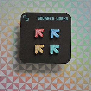 May include: A black square with the text "SQUARES. WORKS" and four arrow-shaped pins in red, blue, yellow, and teal. The pins are arranged in a 2x2 grid. The background is a holographic pattern.