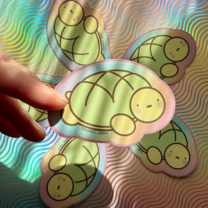 May include: A collection of turtle-shaped stickers with a pastel color scheme. Each sticker features a light green turtle design with a yellow face and a pink and blue border. The text "SQUARES. WORKS" is printed on each sticker.