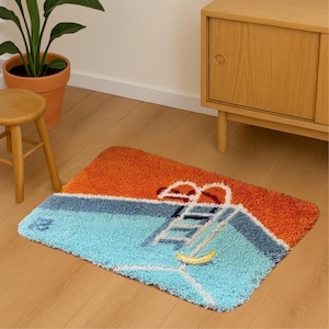 Puede incluir: Una alfombra de baño rectangular con diseño de piscina. La alfombra presenta una piscina azul con una escalera, un flotador de piscina amarillo y un cielo naranja. Sandalias rojas en la parte superior de la alfombra. La alfombra es de material suave y texturizado.