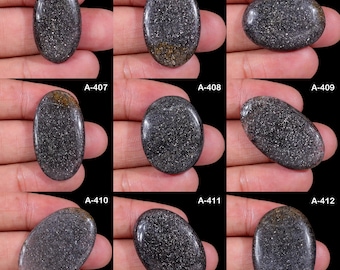 May include: A collection of nine oval-shaped black sunstone cabochons with shimmering metallic inclusions. Each stone is labelled with a code from A-404 to A-412, showcasing a polished, reflective surface with varying dark grey and charcoal tones.