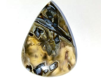 May include: A polished, teardrop-shaped gemstone. The stone displays a mix of colours, including tan, brown, black, and white, with a translucent quality. The pattern within the stone has a layered appearance, with streaks and inclusions.