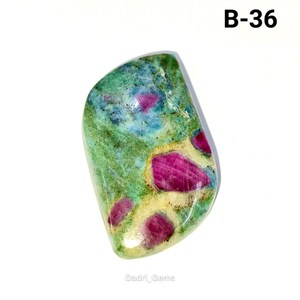 May include: A polished gemstone with a mix of colors. The stone features a base of green and blue hues, with vibrant red patches scattered throughout. The text "B-36" is visible in the upper right corner. The gemstone is likely used for jewelry or collection.