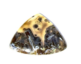May include: A triangular gemstone with a polished surface. The stone displays a mix of tan, brown, and black hues, with distinctive patterns and inclusions. The gemstone is set against a white background.