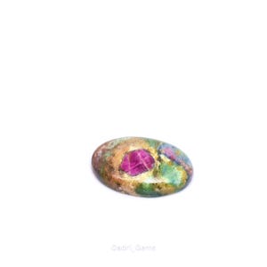 Peut inclure: Une pierre précieuse ovale avec un centre rose vif et une surface mouchetée de nuances vertes, brunes et bleues. La pierre est posée sur un fond blanc, mettant en valeur ses couleurs et textures naturelles. Un bijou unique.