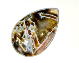 May include: A polished, teardrop-shaped gemstone. The stone displays a mix of brown, white, and tan hues with complex patterns. The gemstone is set against a white backdrop. The text "Qadri_Gems" is visible at the bottom of the image.