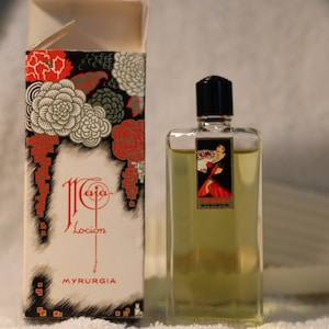 Może przedstawiać: Winietka perfum Myrugia Caja Locion z czarną nakrętką i ozdobną etykietą przedstawiającą kobietę w czerwonej sukni. Pudełko ma kwiatowe wzory w kolorze czerwonym, białym i czarnym.
