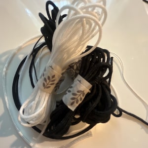 May include: Bundles of black and white cord, tightly wound and secured with decorative paper bands featuring a leaf pattern. The cords are arranged on a white surface, with some strands extending outwards.