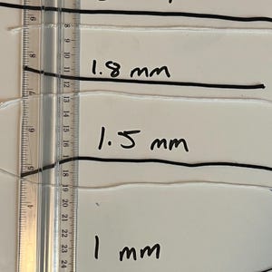 May include: Image shows four strands of cord, each with a different diameter, measured with a ruler. The diameters are labeled as 2 mm, 1.8 mm, 1.5 mm, and 1 mm. The cords are black and white.