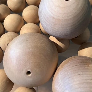 May include: A collection of unfinished wooden spheres with a natural, light brown color. Each sphere has a small, drilled hole. The spheres vary slightly in size and are arranged closely together, suggesting they are craft supplies.