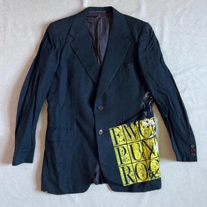 Könnte beinhalten: Dunkelblauer Blazer mit gelb-schwarzer Grafik auf der Vorderseite. Die Grafik zeigt "ENG PUNK ROCK" in Blockbuchstaben. Der Blazer hat zwei Knöpfe und drei Knöpfe am Ärmel.