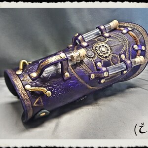 May include: A purple leather steampunk arm cuff with gold accents and clear glass tubes. The cuff has a decorative design with a circular pattern and rivets.