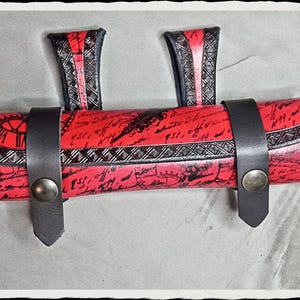 Pode incluir: Um rolo de couro vermelho com tiras pretas e um design decorativo. O rolo tem um visual vintage e é perfeito para guardar canetas, lápis ou outros itens pequenos.