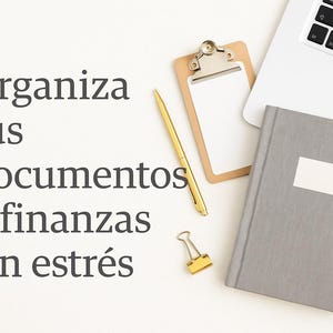 May include: A workspace setup featuring a laptop, a gray notebook with a white label, a wooden clipboard, a gold pen, and a gold binder clip. The image includes the text "Organiza tus documentos y finanzas sin estr&eacute;s."