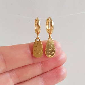 May include: A pair of gold hoop earrings with a textured teardrop charm hanging from each hoop.