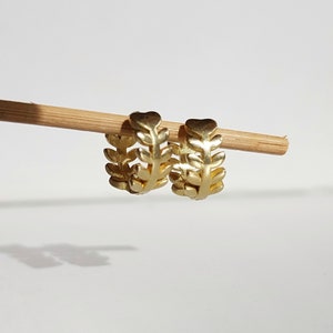 May include: A pair of gold hoop earrings with a leaf design. The earrings are made of metal and have a delicate, feminine look.