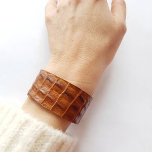 May include: A brown leather bracelet with a crocodile pattern.