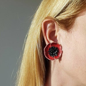 Könnte beinhalten: Ein roter Leder-Mohnblumenring und passende Ohrringe. Der Ring hat eine schwarze Mitte und die Ohrringe haben eine schwarze Mitte.
