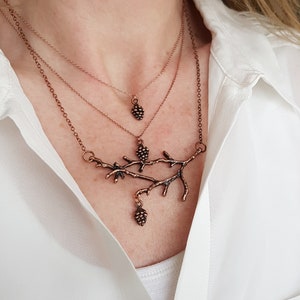 May include: A layered copper necklace with a delicate branch design and three small pine cone pendants.