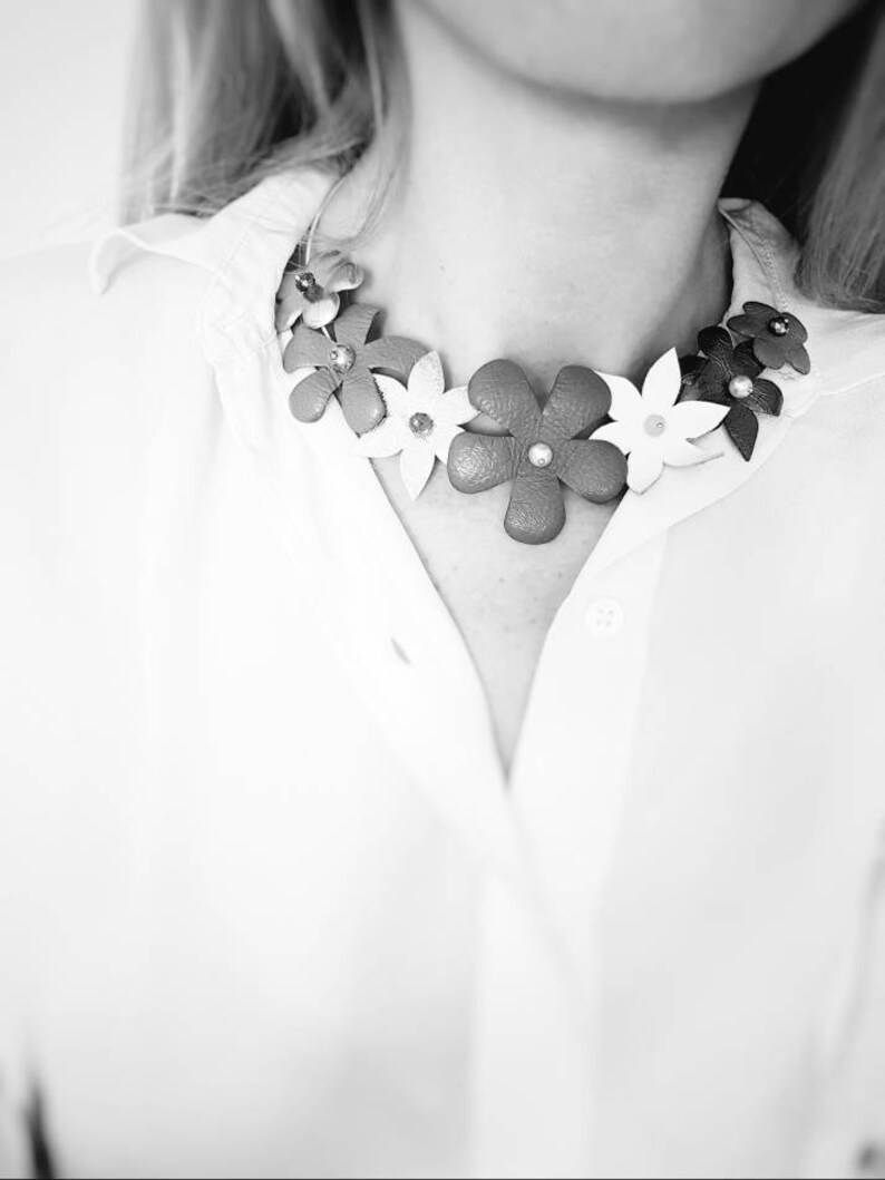Peut inclure: Un chemisier blanc avec un collier de fleurs en cuir. Le collier est compos&eacute; de fleurs blanches, rouges et brunes.