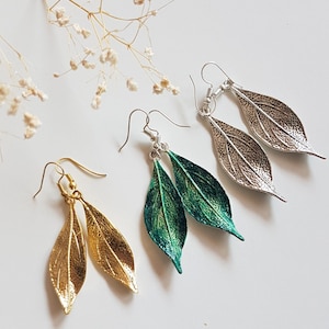 Puede incluir: Tres pares de pendientes en forma de hoja en oro, verde y plata. Los pendientes son todos de metal y tienen un acabado texturizado.