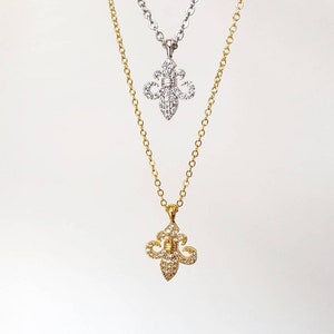 May include: Two gold necklaces with a fleur-de-lis pendant. Both pendants are encrusted with clear cubic zirconia stones.