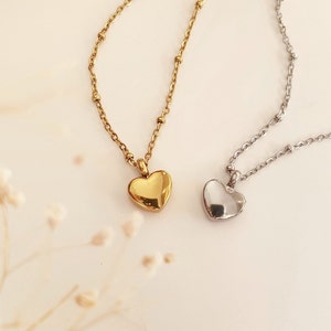 以下が含まれることがあります： ハート型のペンダントネックレスが2つ。一つは金色、もう一つは銀色です。どちらも、小さく均等に配置されたビーズが付いた繊細なチェーンが付いています。ペンダントは滑らかで光沢があり、光を反射します。