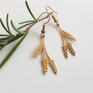 Può includere: Un paio di orecchini dorati con un design delicato che presenta un rametto di foglie e grano. Gli orecchini sono appesi a un semplice gancio.
