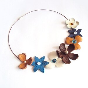 Peut inclure: Un collier en cuir marron avec une vari&eacute;t&eacute; de fleurs en cuir color&eacute;es. Les fleurs sont d&eacute;cor&eacute;es de petites perles et sont dispos&eacute;es en cercle autour du collier.
