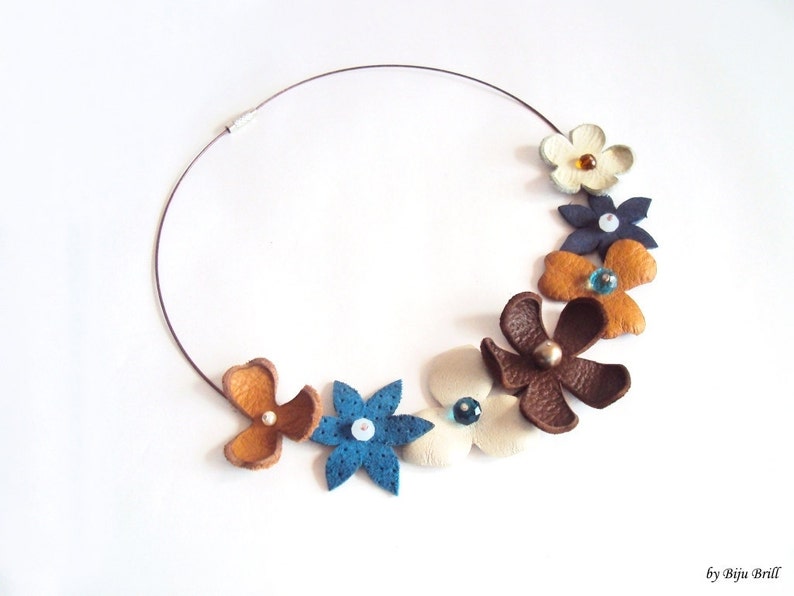 Peut inclure: Un collier en cuir marron avec une vari&eacute;t&eacute; de fleurs en cuir color&eacute;es. Les fleurs sont d&eacute;cor&eacute;es de petites perles et sont dispos&eacute;es en cercle autour du collier.