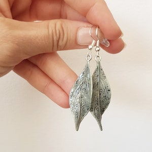 May include: Silver leaf earrings with a textured surface. The earrings are hanging from silver hooks.