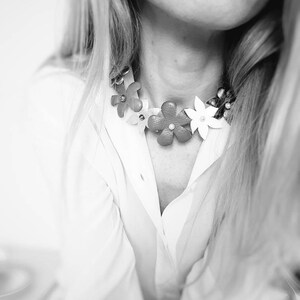 Peut inclure: Gros plan d'une femme portant une chemise blanche avec un collier ras de cou floral. Le collier est en cuir et pr&eacute;sente des fleurs color&eacute;es.
