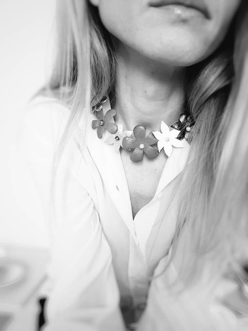 Peut inclure: Gros plan d'une femme portant une chemise blanche avec un collier ras de cou floral. Le collier est en cuir et pr&eacute;sente des fleurs color&eacute;es.