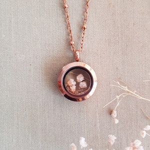 May include: Rose gold locket necklace with a delicate chain and a clear glass locket containing dried flowers.