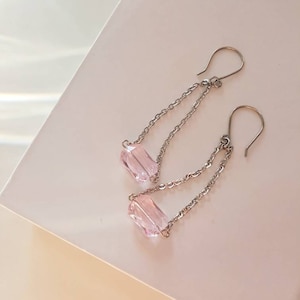 May include: A pair of silver chain earrings with pink crystal drops. The earrings have a simple design and are perfect for everyday wear.