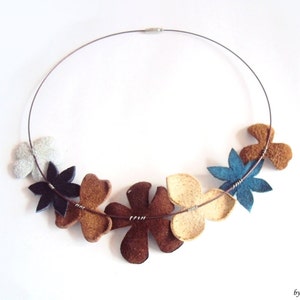 Peut inclure: Un collier en fil d'argent avec sept breloques en forme de fleurs en feutre dans des tons de brun, beige, bleu et blanc.