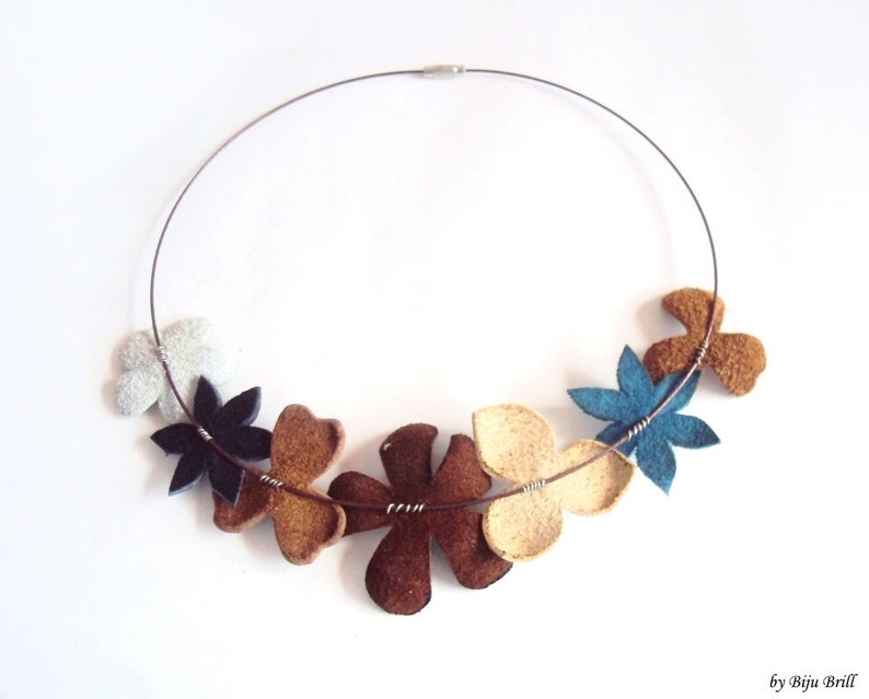 Peut inclure: Un collier en fil d'argent avec sept breloques en forme de fleurs en feutre dans des tons de brun, beige, bleu et blanc.
