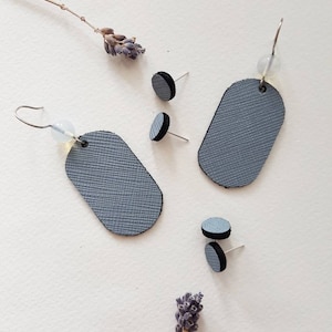 以下が含まれることがあります： グレーの革製のイヤリング3つのセット。2つのイヤリングは楕円形で、シルバーのフックが付いています。3つ目のイヤリングは、シルバーのポストが付いた小さな円形です。