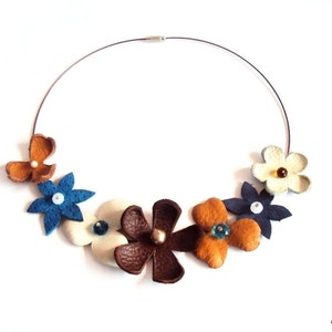 Peut inclure: Un collier de fleurs en cuir avec des fleurs brunes, bleues, blanches et orange. Le collier est fait avec un fil d'argent et a une vari&eacute;t&eacute; de perles color&eacute;es au centre de chaque fleur.