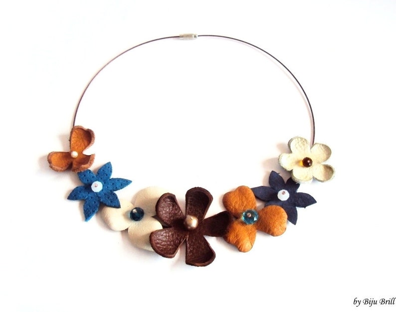 Peut inclure: Un collier de fleurs en cuir avec des fleurs brunes, bleues, blanches et orange. Le collier est fait avec un fil d'argent et a une vari&eacute;t&eacute; de perles color&eacute;es au centre de chaque fleur.
