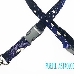 May include: A purple and black lanyard with a white star and moon pattern. The lanyard has a black plastic clip and a silver metal hook. The text "PURPLE ASTROLOGY" is printed on the lanyard.