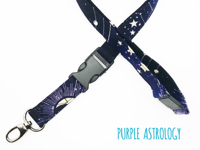 May include: A purple and black lanyard with a white star and moon pattern. The lanyard has a black plastic clip and a silver metal hook. The text "PURPLE ASTROLOGY" is printed on the lanyard.
