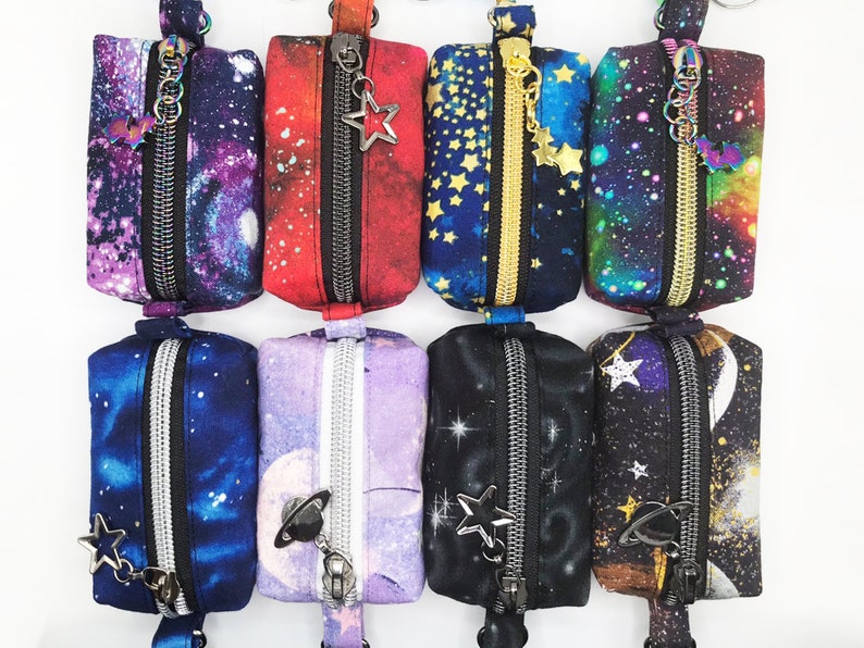 K&ouml;nnte beinhalten: Acht kleine Rei&szlig;verschlusstaschen mit Galaxie-Druck. Die Taschen sind aus Stoff und haben einen Rei&szlig;verschluss. Jede Tasche hat eine andere Farbe und ein anderes Design. Die Taschen sind perfekt zum Verstauen von kleinen Gegenst&auml;nden wie Schl&uuml;sseln, M&uuml;nzen oder Schmuck.
