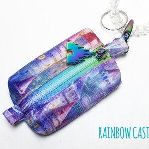 May include: A small purple and blue zippered pouch with a rainbow castle print. The pouch has a rainbow castle charm attached to a clear plastic keychain.
