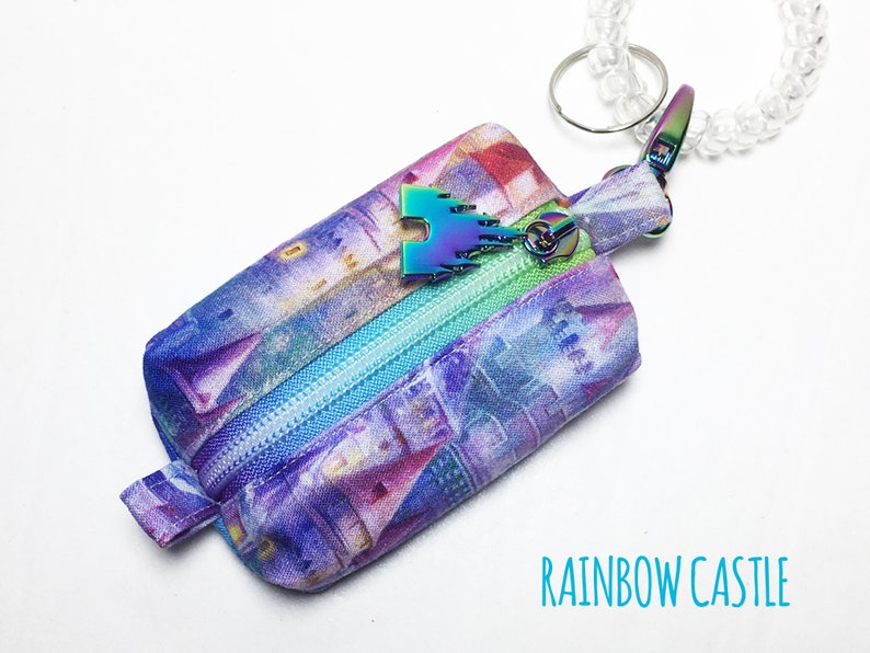 May include: A small purple and blue zippered pouch with a rainbow castle print. The pouch has a rainbow castle charm attached to a clear plastic keychain.