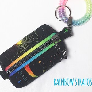 May include: A small black zippered pouch with a rainbow and star pattern. The pouch is attached to a rainbow coiled keychain with a star charm.
