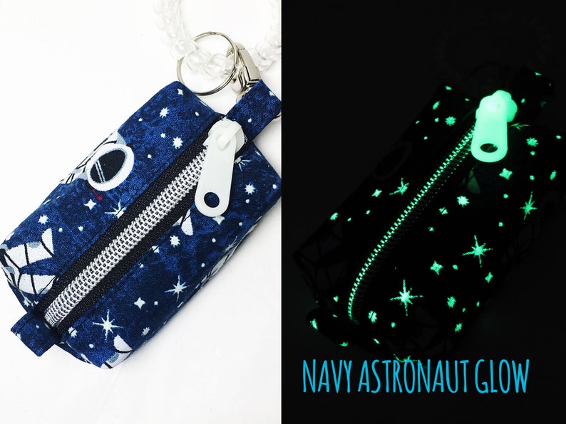 May include: A small blue zippered pouch with a white zipper pull and a white astronaut design. The pouch is decorated with white stars and glows in the dark. The text "NAVY ASTRONAUT GLOW" is printed below the pouch.