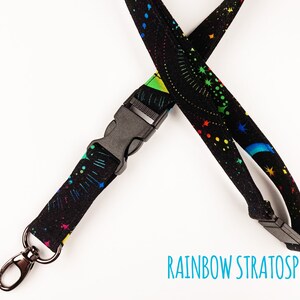 May include: Black lanyard with a rainbow and star pattern. The lanyard has a black plastic clip and a silver swivel hook.